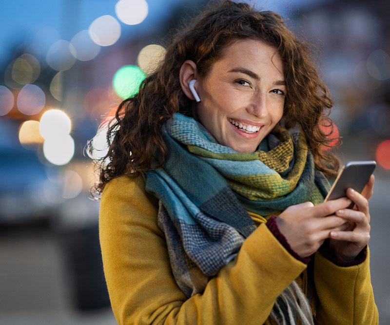 Vinter kvinna i halsduk som ler och håller i en mobil
